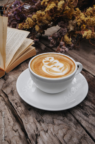 Cappuccino coffee latte art, Warm coffee in mug on white plate with Dried flowers background.