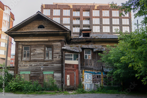 Old wooden rundown house with patched doors and windows against the background of a new house under construction
