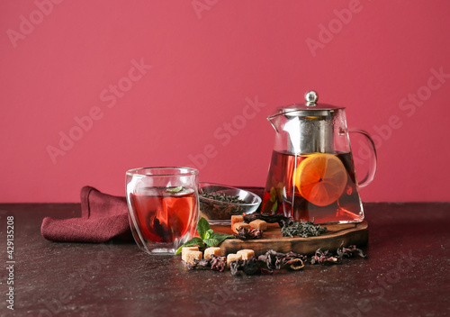 Teapot and glass of tasty black tea with lemon and mint on color background