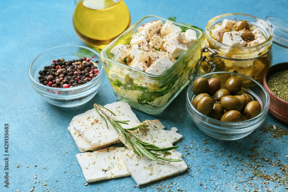 Bowls and jar with tasty feta cheese, oil and olives on color background