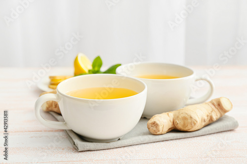 Cups of tea with ginger, mint and lemons on light wooden background