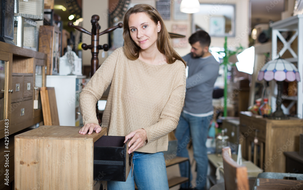 Happy young woman looking for stylish small cabinet in shop of secondhand furniture