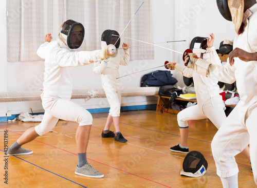 Adults and teens wearing fencing uniform practicing with foil in gym