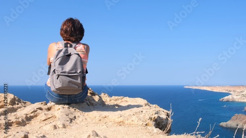 Young happy woman with a backpack sits on a rock and looks at the valley below.The concept of freedom and ease