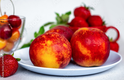 still life of nectarines with ripe summer berries, healthy nutrition concept, autumn harvest of fruit on blue plate closeup