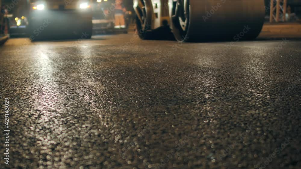 Strong plan of freshly laid asphalt. Two road rollers are laying asphalt. Steam from hot asphalt. Road repair in the city at night. Strong plan of freshly laid asphalt. Two road rollers are laying asphalt. Steam from hot asphalt. Road repair in the city at night.