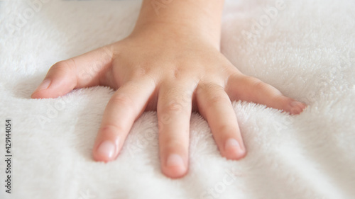 Closeup of left hand of a little girl placed on a white soft and cozy blanket