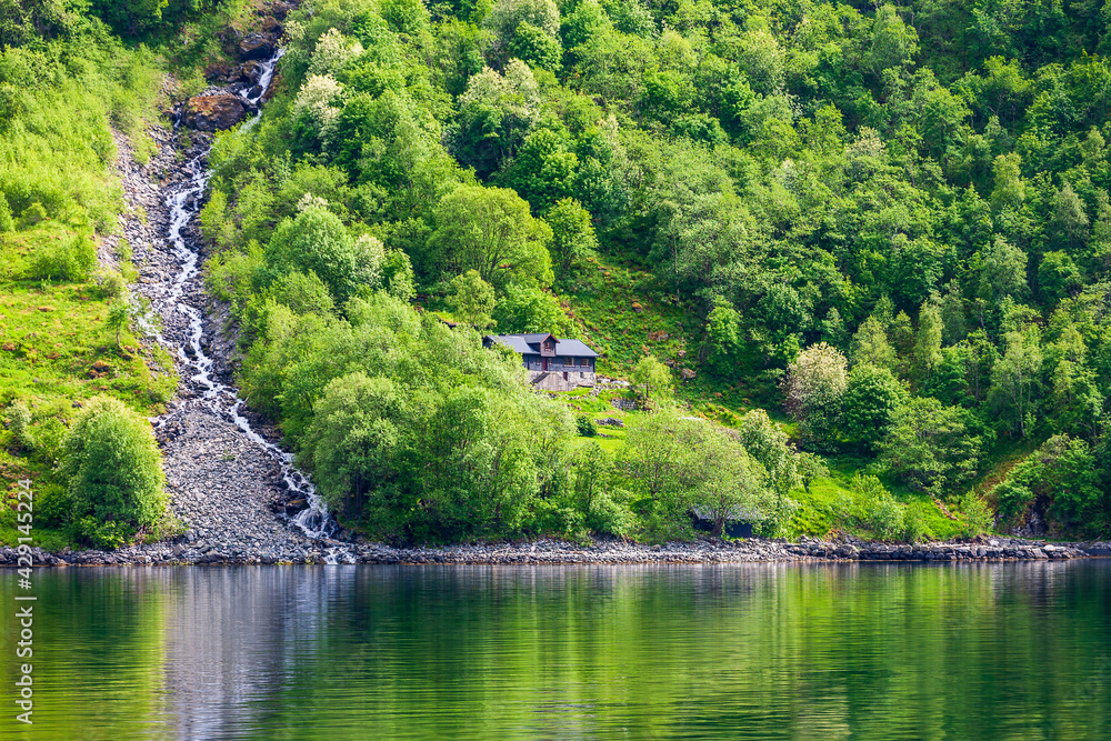 Small cottage by a waterfall on the shore of a fjord