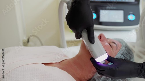 Woman receiving HUFU therapy- high intensity focused ultrasound treatment on face. Therapist doing non-surgical cosmetic plasma lift on female client forehead with ultrasonic device.