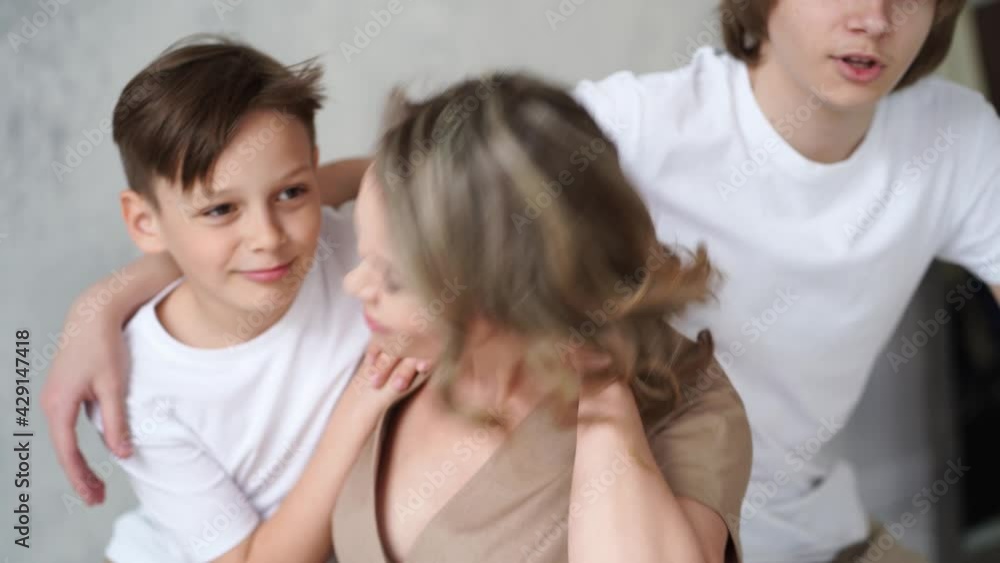 A mother and sons in beige and white clothes pose on the chair for a photo shoot A mother and sons in beige and white clothes pose on the chair for a photo shoot