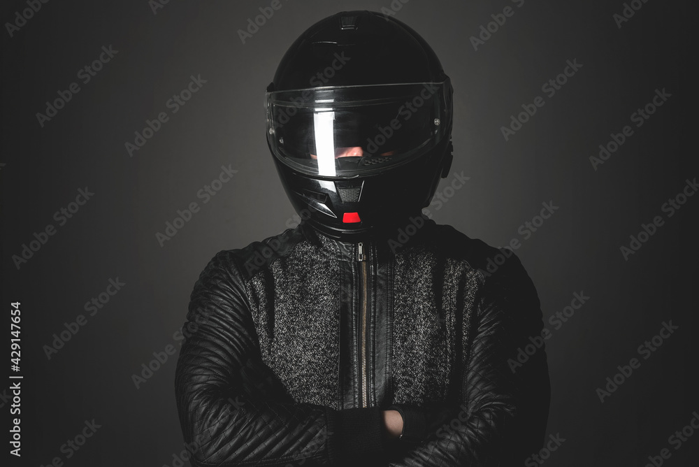 Serious motorbiker in a helmet with a crossed arms is standing on the dark background.