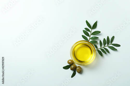 Bowl of oil, olives and twigs on white background