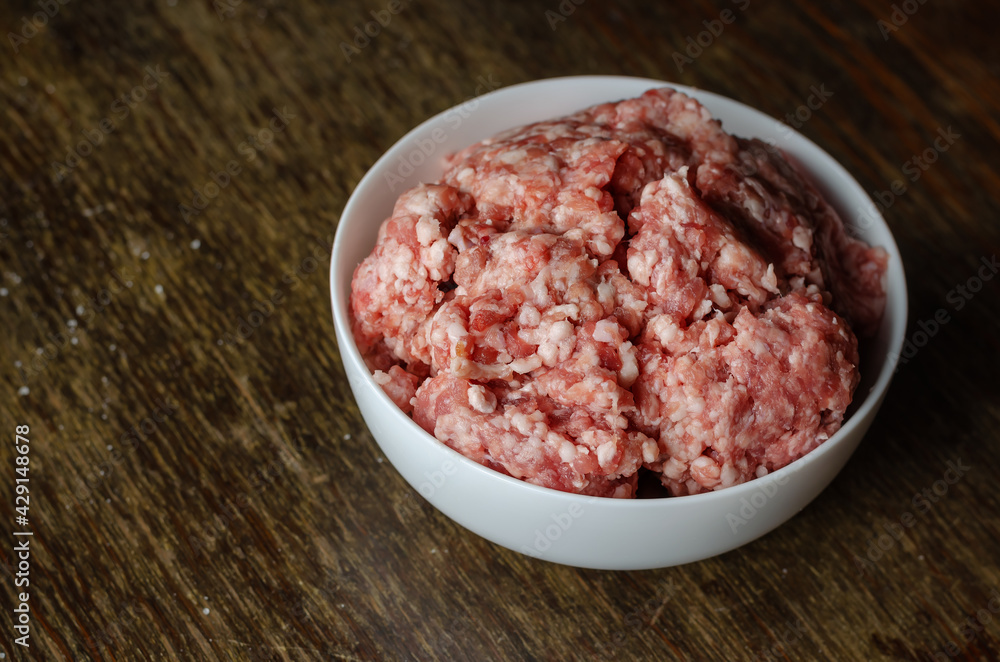 White ceramic bowl with raw minced meat on a dark wooden table. White ceramic bowl with raw minced meat on a dark wooden table.