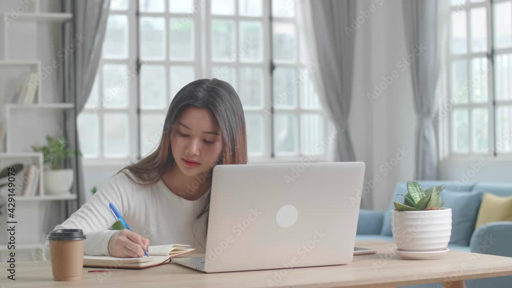 Working From Home, Asian Girl Using Laptop Computer And Writing On Notebook Working From Home, Asian Girl Using Laptop Computer And Writing On Notebook