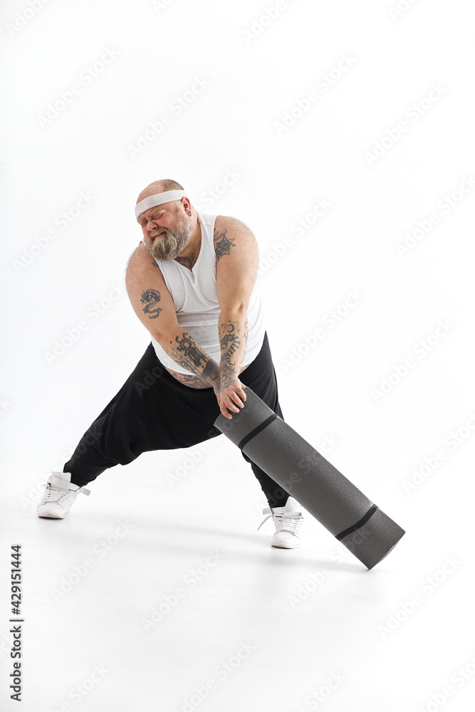 Obraz premium Happy fat man with big belly and tattos in sports wear with exercise mat