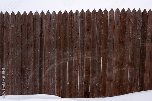 A fence made of sharp wooden planks against a cloudy sky and standing in the snow. photo