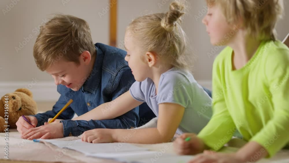 Side view of joyful Caucasian children drawing lying in living room at home. Positive carefree boys and girl enjoying leisure indoors. Creativity and talent concept Side view of joyful Caucasian children drawing lying in living room at home. Positive carefree boys and girl enjoying leisure indoors. Creativity and talent concept