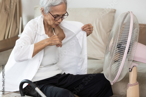 фотографія Sweaty asian senior woman opening shirt,cooling herself in front of a fan,stay a
