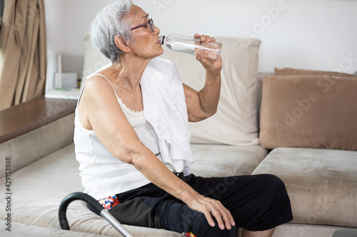 Thirsty senior woman suffering from heat,drinking fresh water from a bottle to quench their thirst in hot summer weather,high temperature on a sunny day,feeling thirsty,water balance,lifestyle concept