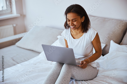 Joyful young woman using modern laptop at home