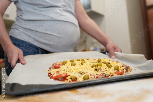 Pregnant woman holds on a baking sheet prepared for baking healthy gluten-free pizza with beef. Gluten-free cooking class. Cooking at home. 