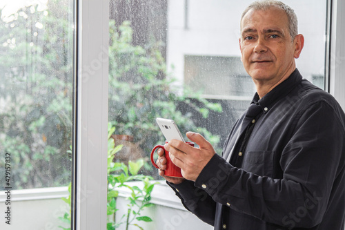 adult man having a cup of coffee at office or home while using the phone