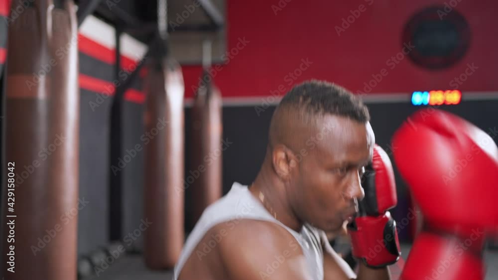 Africa American or athletic man wearing boxing glove doing boxing with trainer or coach in the fitness gym. Exercise indoor sport equipment. Punches and moving body. Workout lifestyle