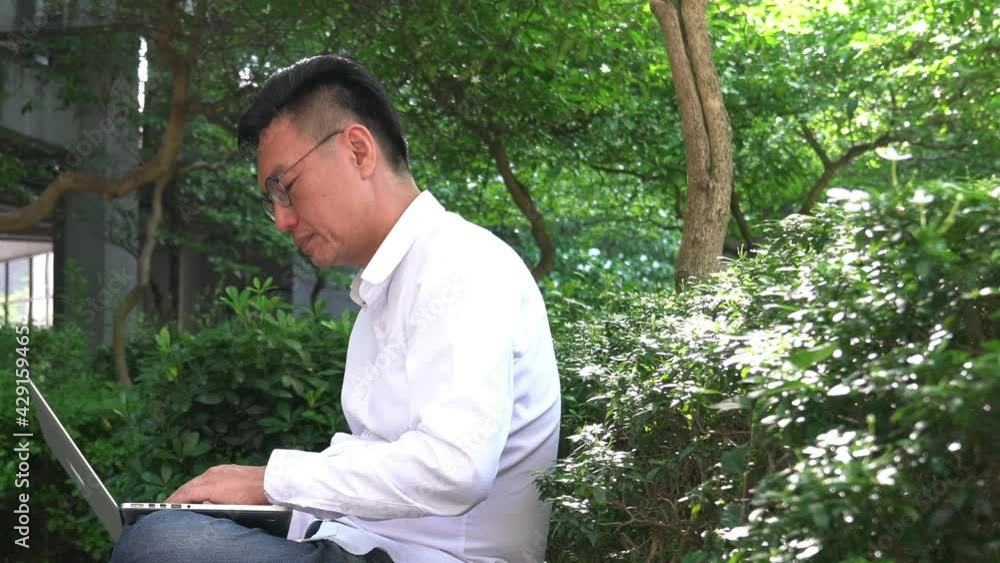 Businessman typing and working on his computer laptop in a green park, outdoors. Remote working concept. Businessman typing and working on his computer laptop in a green park, outdoors. Remote working concept.