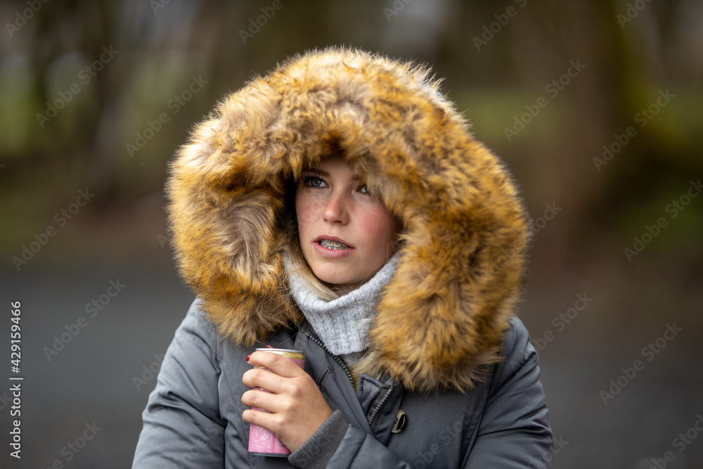 Woman girl young, with a fur hood over her head and braces holds a beverage can in her hand and speaks..