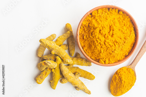 Dry turmeric or haldi powder in a earthen bowl with turmeric roots on white isolated background.
