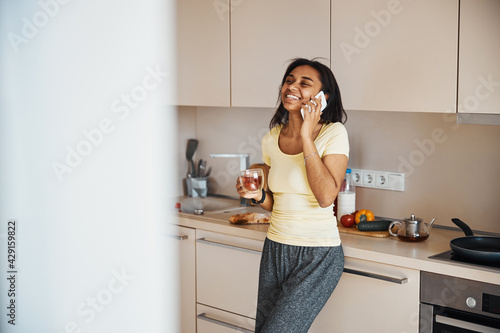 Joyful young woman talking on mobile phone at home