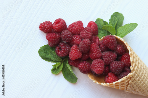Raspberry in waffle cone on white wooden table.