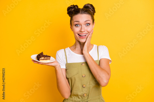 Portrait of impressed brunette nice lady hold piece of cake wear bright t-shirt overall isolated on vivid yellow color background
