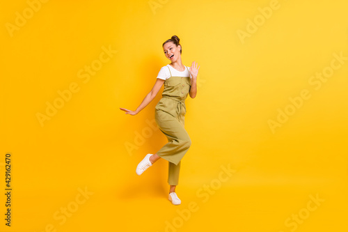 Photo of funny carefree lady dance look side open mouth wear green overall shoes isolated yellow background
