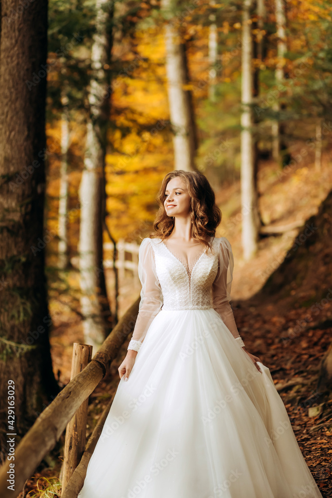 Pretty bride with wavy hair walks on a trail in autumn park.