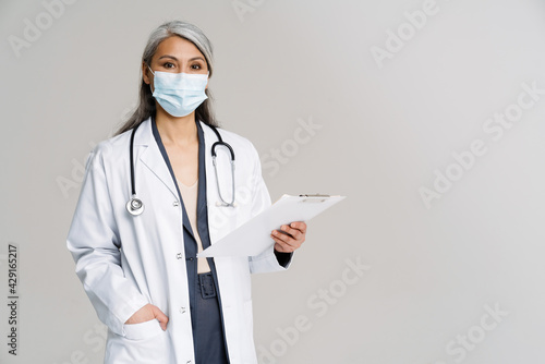 Asian mature woman in medical uniform and mask holding notepad