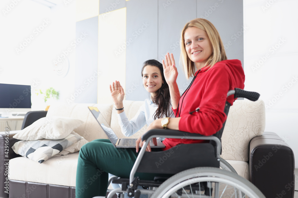 Woman in wheelchair sitting with laptop and waving hand Woman in wheelchair sitting with laptop and waving hand