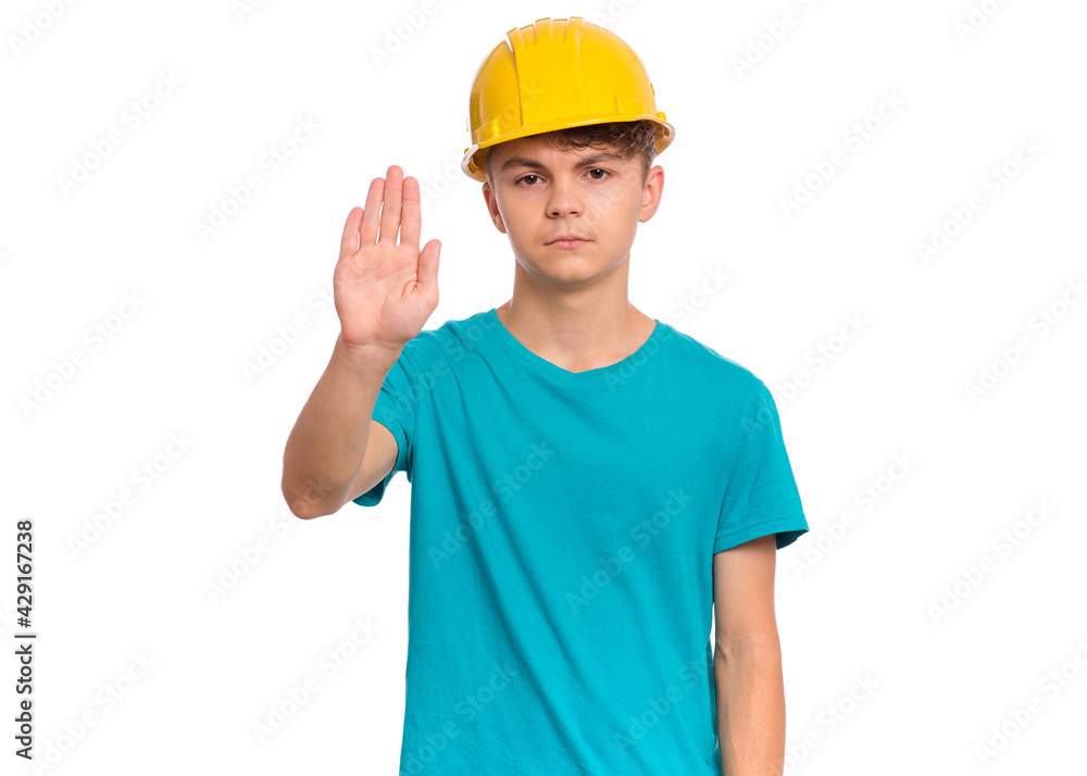 Handsome Teen Boy wearing yellow Hard Hat doing stop sign with palm of hands. Portrait of serious Child making stop gesture and Looking at camera, isolated on white background