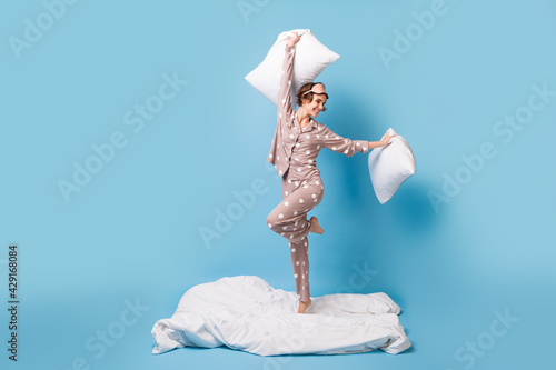 Full size photo of young charming lovely happy excited girl dancing on blanket hold pillows isolated on blue color background