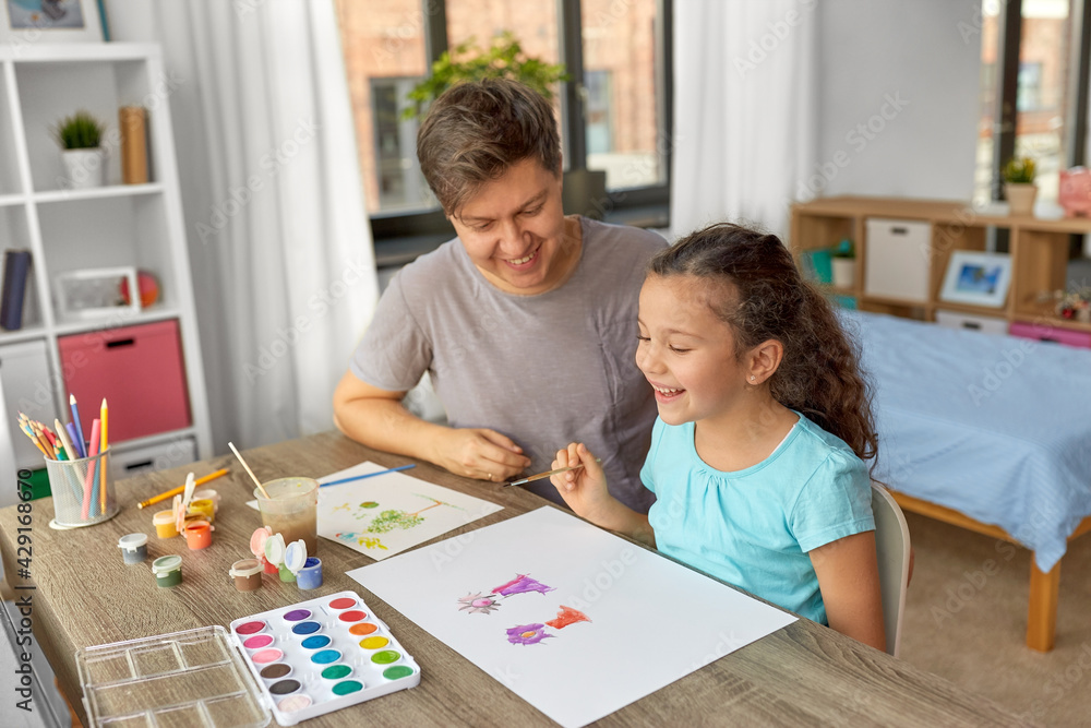 family, motherhood and leisure concept - happy smiling father spending time with his little daughter and drawing with colors at home