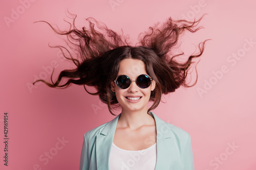 Joyful excited surprised young woman with flying hair wear blazer sunglass on pink wall
