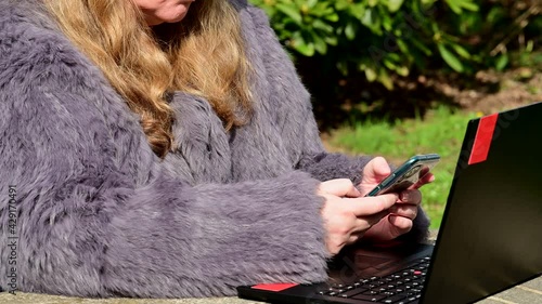 Frau in einer Kaninchenfell Jacke arbeitet im Garten mit einem Notebook im Homeoffice  