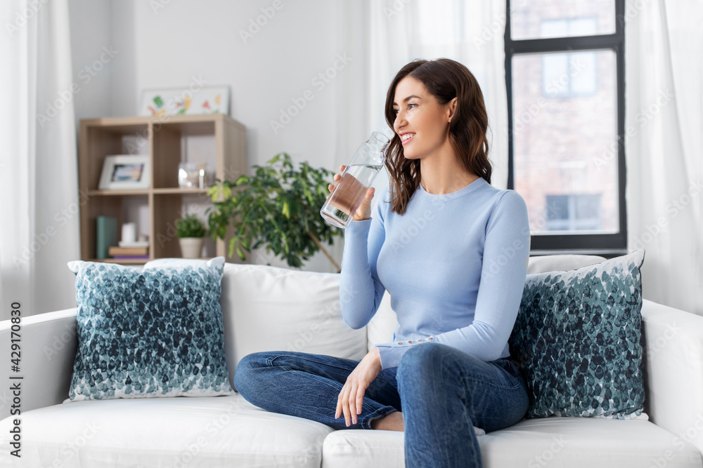 people, sustainability and leisure concept - happy smiling young woman drinking water from glass bottle at home people, sustainability and leisure concept - happy smiling young woman drinking water from glass bottle at home