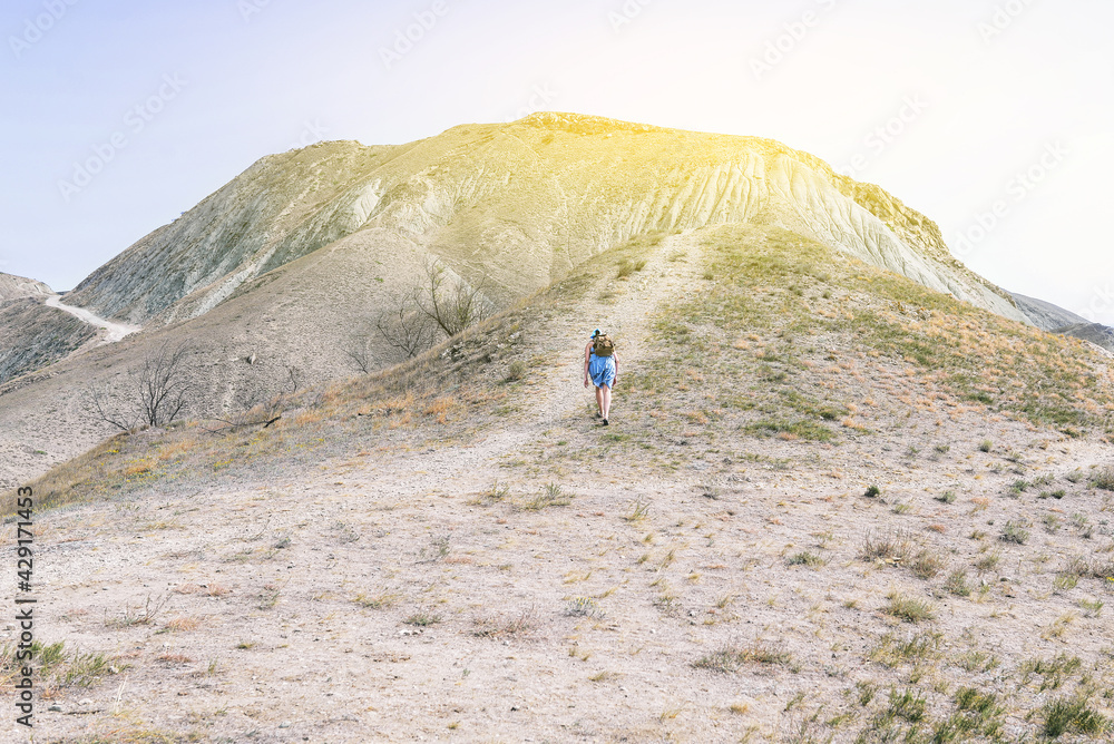 Traveler with a backpack climbs the mountain. Hiking in the mountains on a sunny warm day. Leisure activities. Nature background