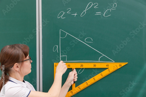 school teacher young woman in the class at the blackboard draws a triangle with a ruler. portrait. close up