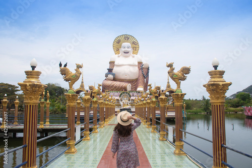 Asian woman tourist sightseeing at Giant smiling or happy buddha statue with blue sky in buddhist temple ( wat plai laem ), Koh Samui, Thailand. photo