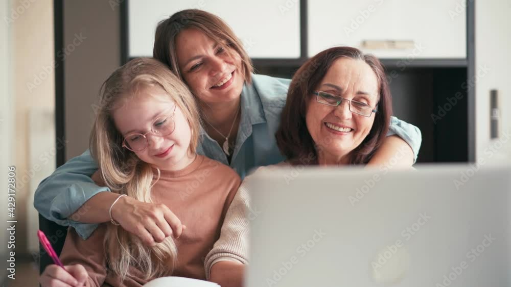 Three generations of a women's part of the family cheerful grandmother, daughter, and a 10-years-old girl waving hands while taking a video call on a laptop. Three generations of a women's part of the family cheerful grandmother, daughter, and a 10-years-old girl waving hands while taking a video call on a laptop.