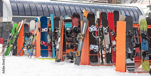 Alpine skis and snowboards leaning on ski rack on snow at winter day photo