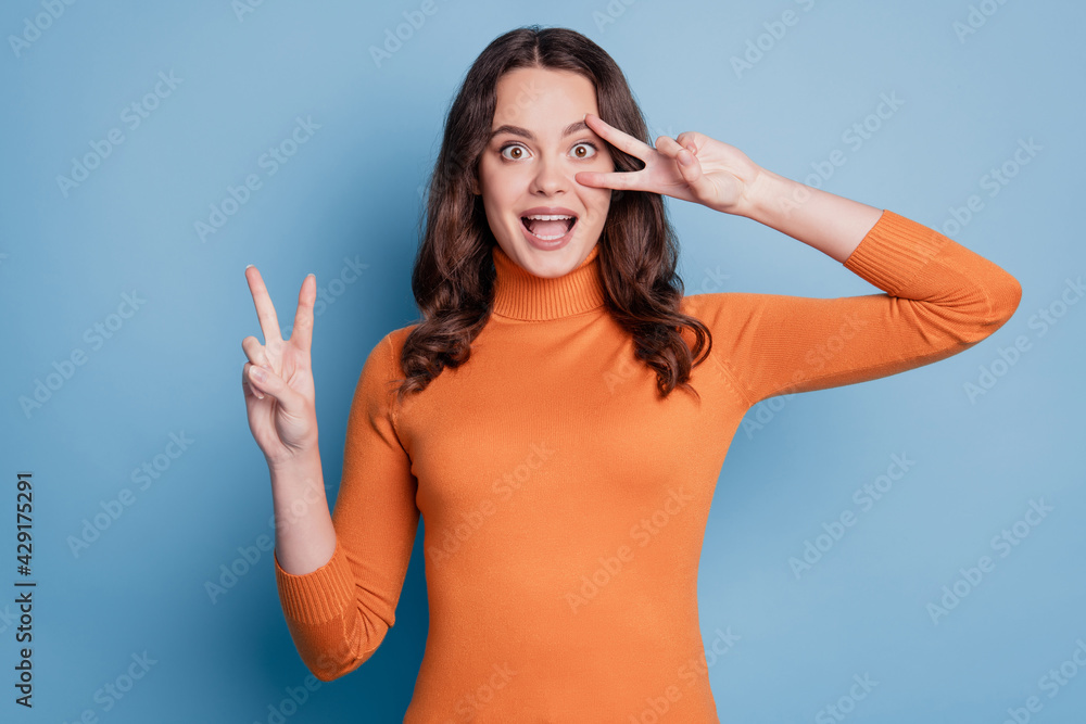 Fototapeta premium Photo of excited cheerful friendly woman on a blue background showing victory sign cover eye