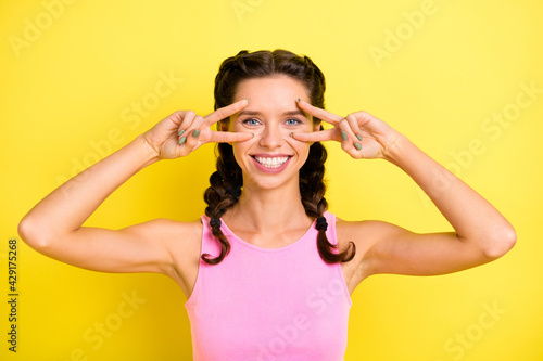Photo of charming sweet young lady braids dressed singlet showing v-sign cover eyes isolated yellow color background
